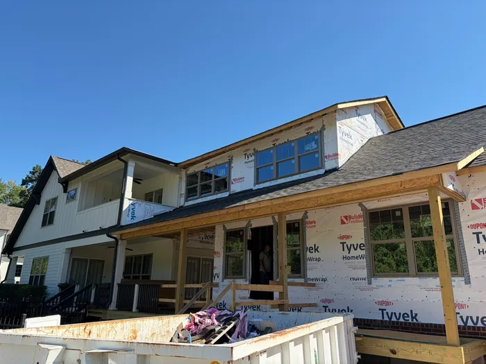 Dried-in addition wrapped in Tyvek with new windows, a shingled roof and a dormer, plus a front porch framed in new lumber, attached to the existing white home
