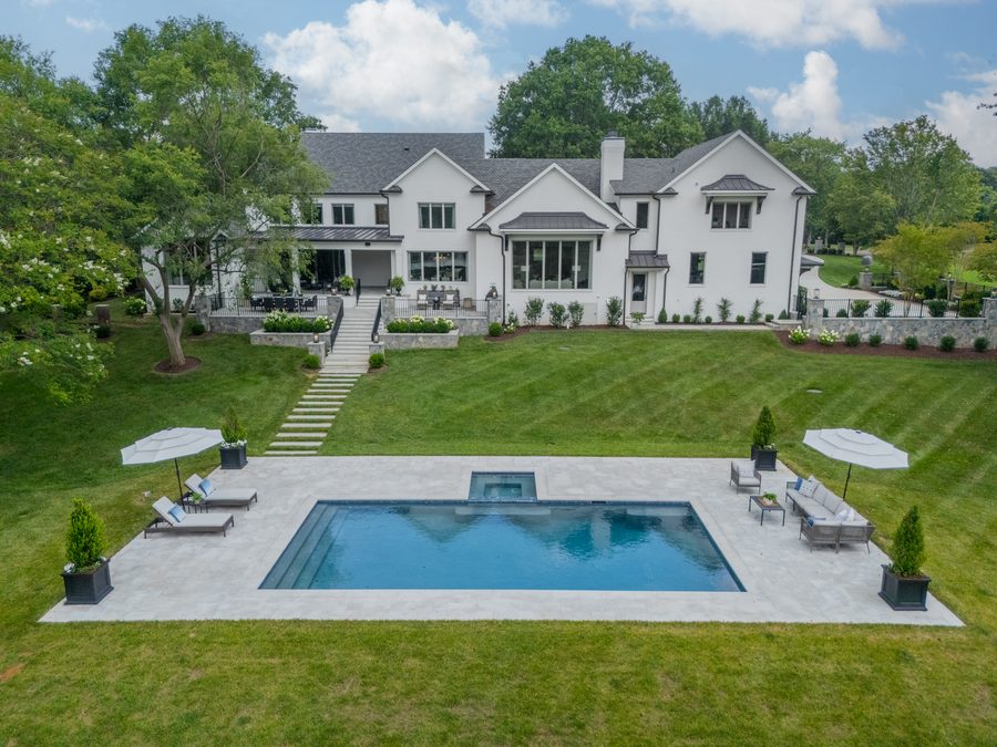 Rear elevation of a custom home with a pool, stone coping, and a broad lawn