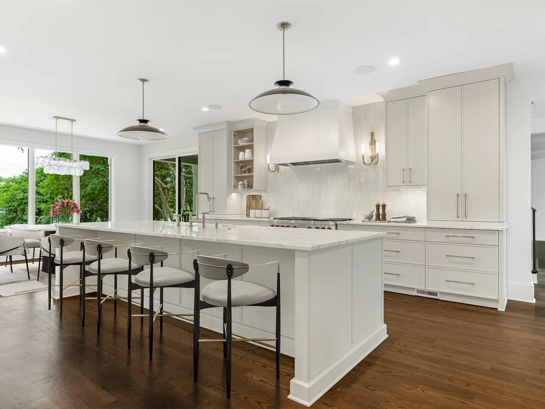 The rebuilt Waldon kitchen with white cabinetry, a long marble island with seating and a plaster range hood