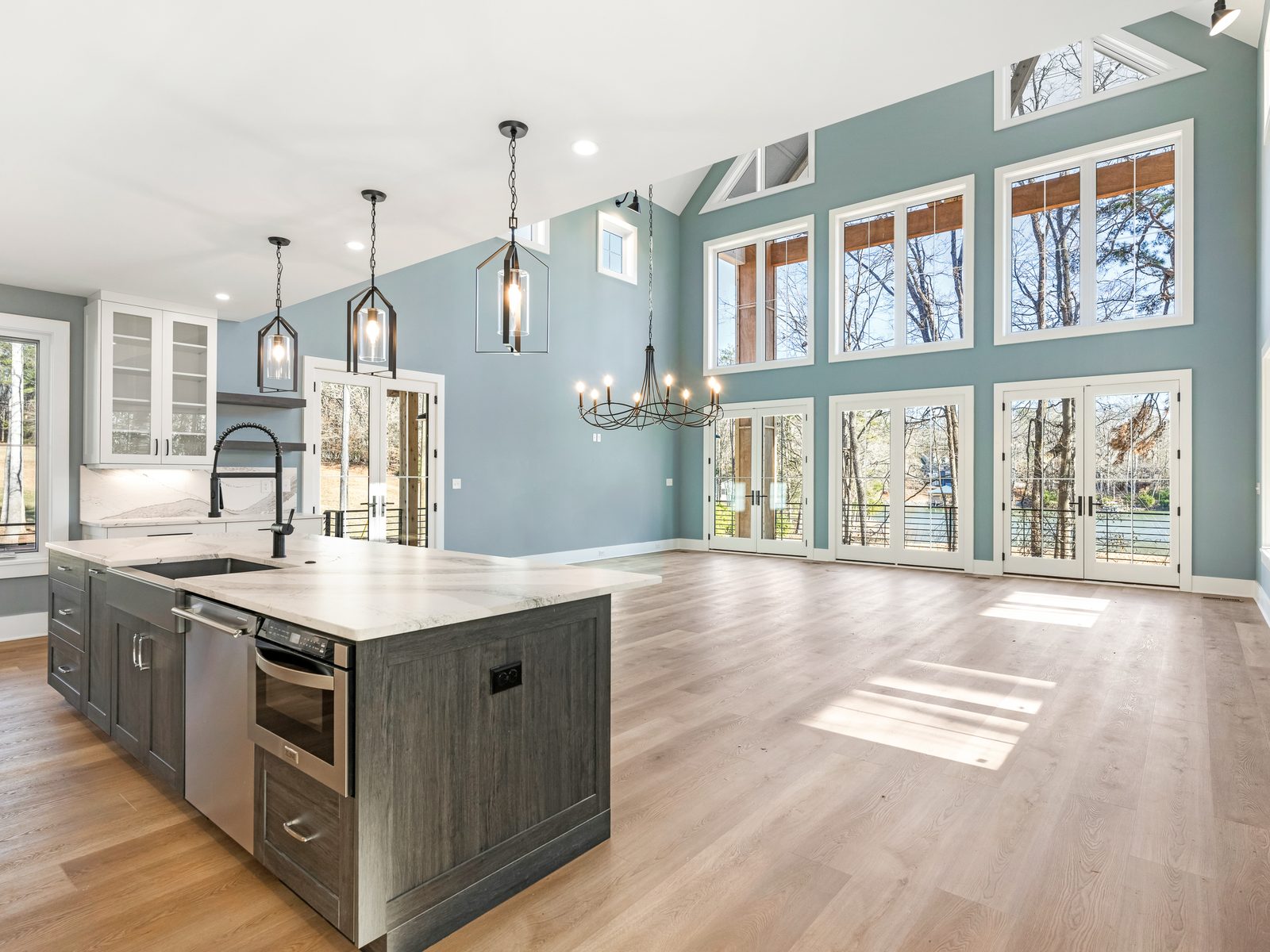A finished open great room and kitchen with a vaulted ceiling, hardwood floors, and a wall of windows, ready for final walkthrough.
