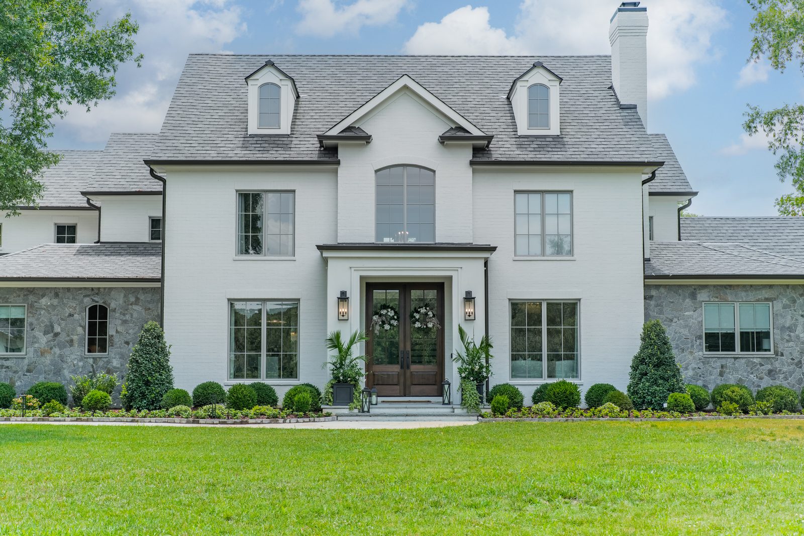 A finished white brick Everett Custom Homes residence with dormers, stone wings, and a double front door, set behind a wide striped lawn.