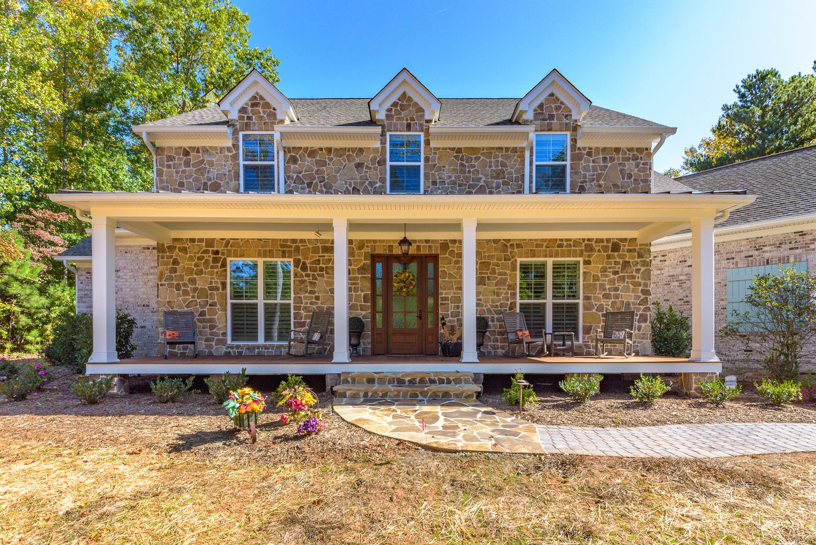 A completed Everett Custom Homes residence with a stone and brick facade, dormers, and a full-width covered front porch.