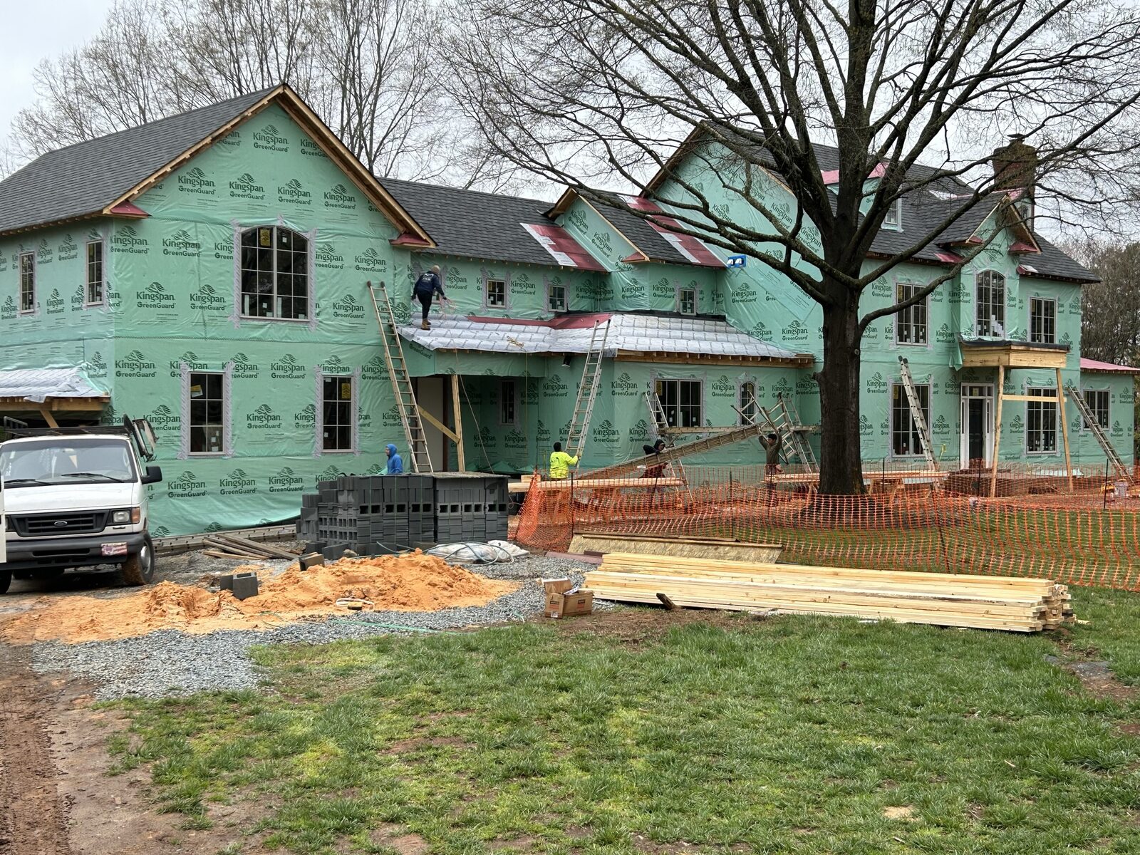 Crews on ladders and the roof installing windows over green Kingspan GreenGuard house wrap across the full width of the rebuilt home.