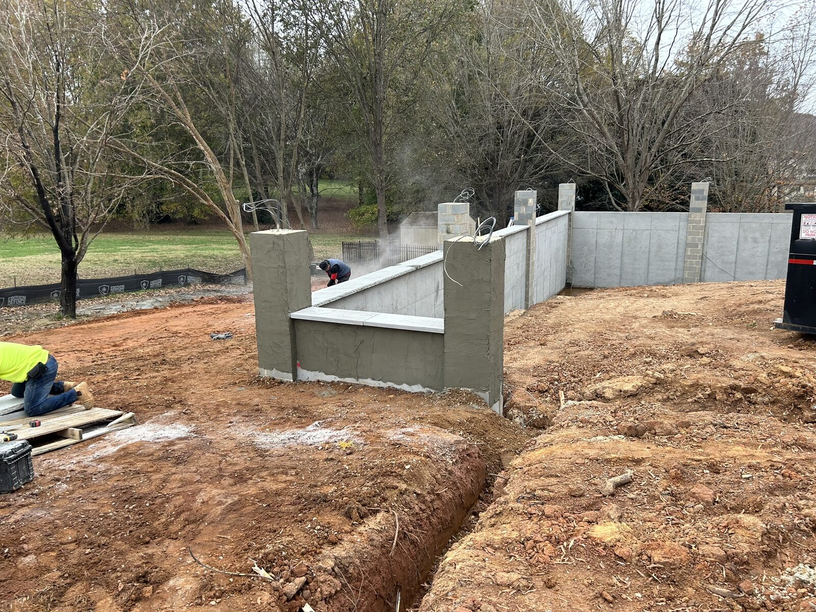 A mason parging the newly built motor court retaining wall, with the stepped concrete wall and pier caps running across the back of the property.