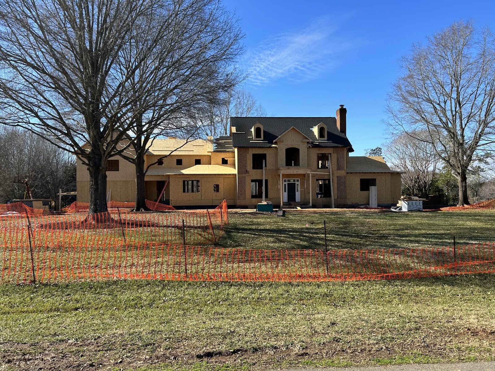 The rebuilt house under construction in winter, sheathed in OSB, with large new window and door openings framed across the front elevation.