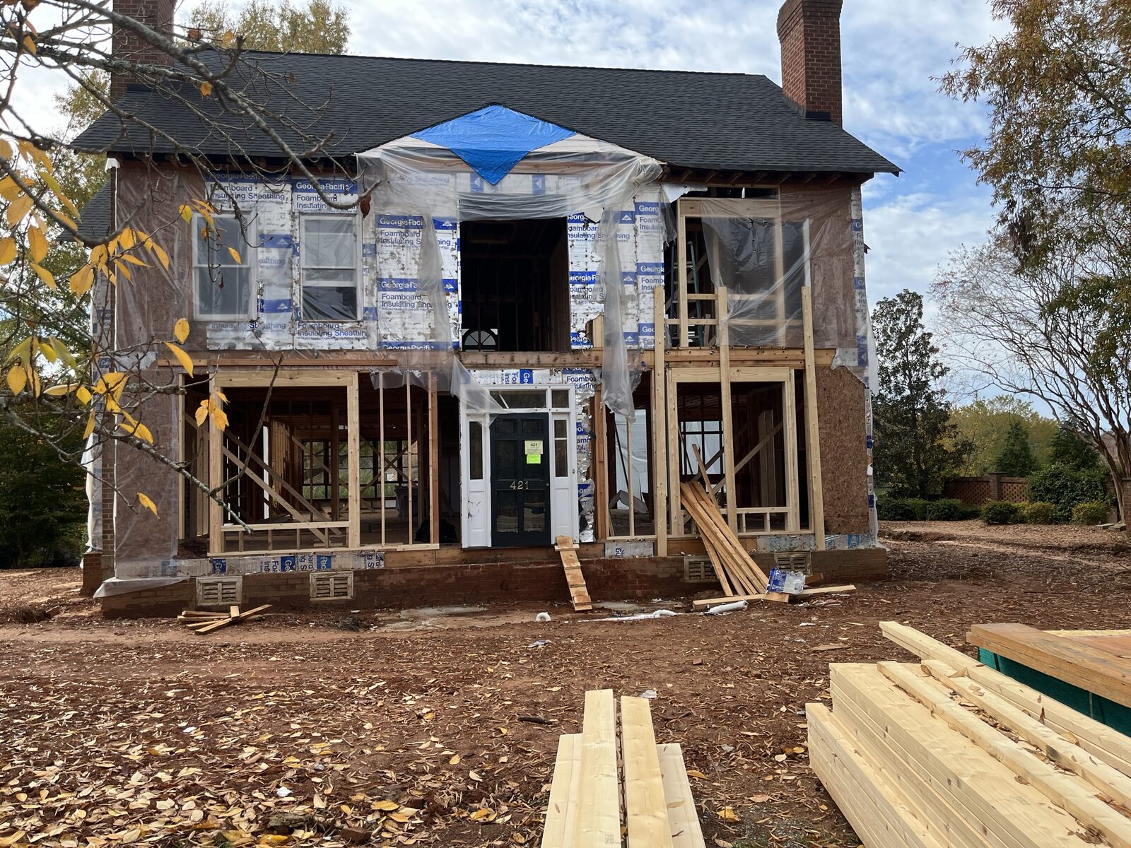 The original 1980s Weddington house stripped to its shell, garage and porches gone, exterior sheathing and foam board exposed with the front porch reframed in new lumber.